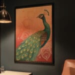 Framed peacock painting on wall in dimly lit room.